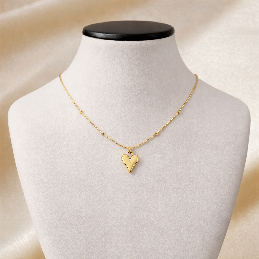 Gold necklace with polished heart pendant on delicate beaded chain displayed on jewelry bust