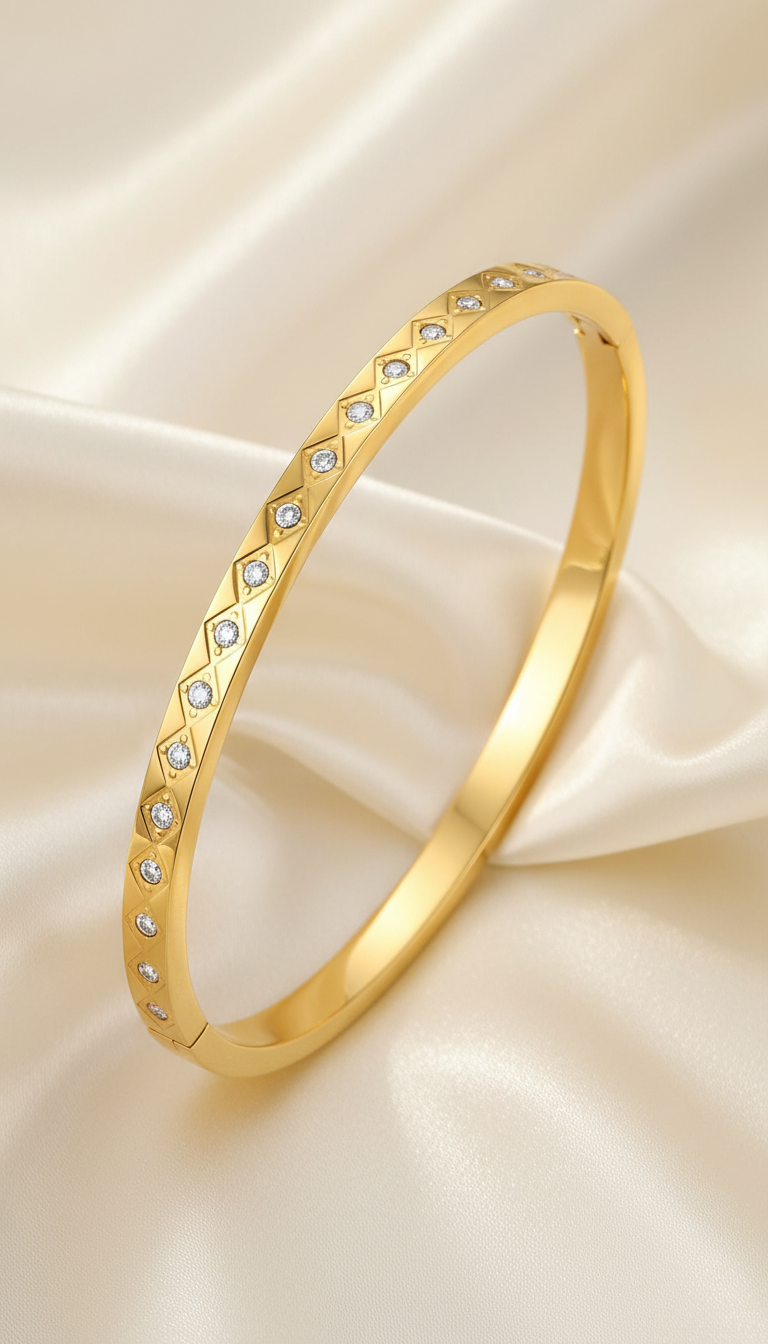 Gold bangle bracelet with engraved diamond grid pattern and cubic zirconia stones on satin background