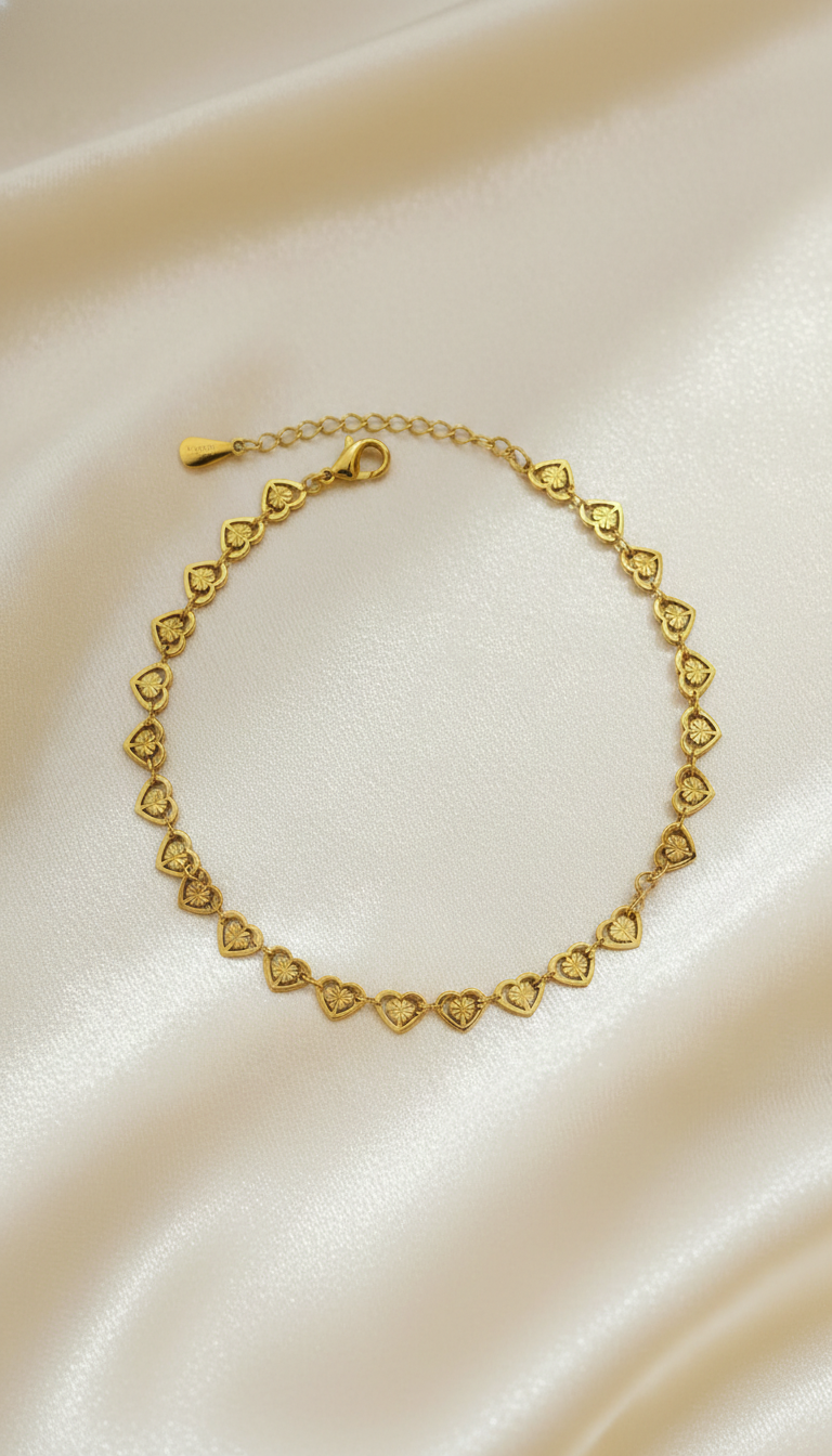 ✨ Bracelet Master Theme – Luxury Editorial Product Prompt A high-resolution, luxurious editorial-style product photograph of a delicate yellow gold chain bracelet featuring small engraved heart-shaped links evenly spaced along the chain. Each heart charm has fine vintage-style detailing, creating a refined and romantic aesthetic. The bracelet includes a polished lobster clasp and a subtle adjustable extension chain, maintaining a lightweight, feminine silhouette. The bracelet is arranged naturally in a soft circular form on luminous ivory satin fabric with warm champagne undertones, viewed from a gently elevated top-down perspective. The chain drapes organically with subtle, natural curves, while the heart charms are evenly spaced and clearly visible. The clasp and extension chain rest delicately toward the upper portion of the composition, maintaining a balanced and elegant layout. The background consists exclusively of softly flowing ivory satin with delicate folds that create smooth gradients and gentle shadows. Lighting is warm, soft, and diffused from the upper left, producing delicate highlights along the polished gold edges and a refined glow across the engraved heart surfaces. The yellow gold reflects a luminous champagne sheen without harsh reflections. Focus is crisp on the central heart charms, with a shallow depth of field that softly blurs the surrounding satin. The overall atmosphere is romantic, refined, and ultra-luxury, suitable for premium fine jewelry branding.