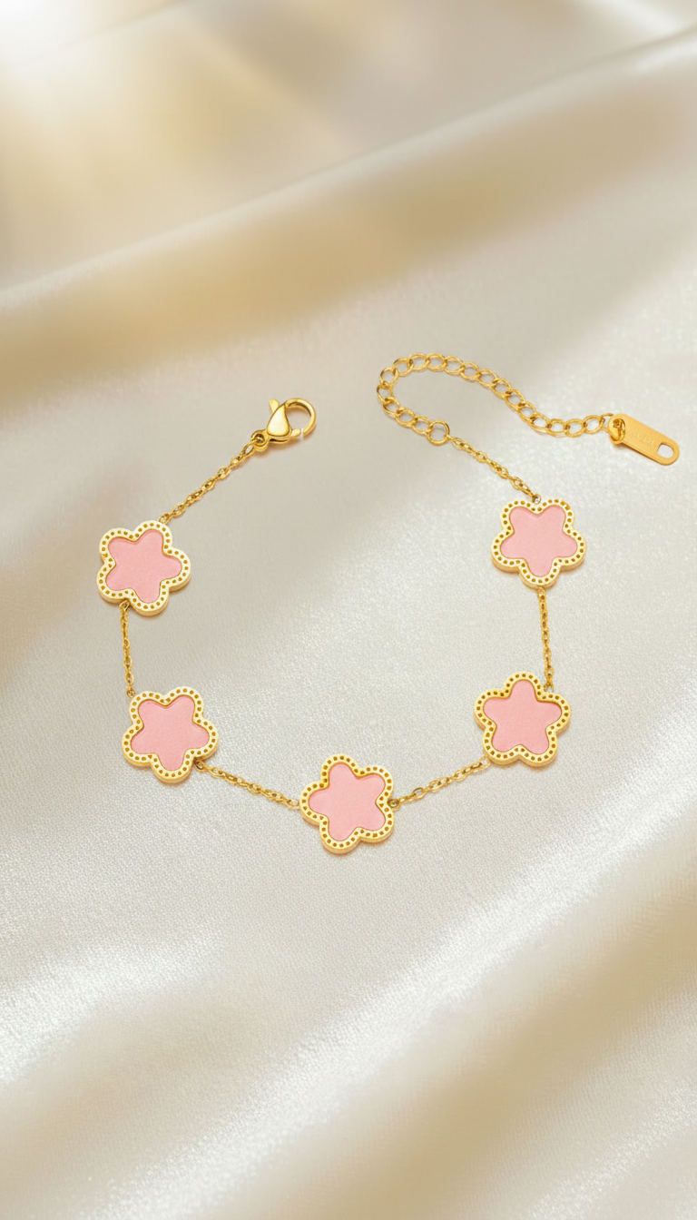 Gold bracelet with five pink enamel clover charms on a delicate chain placed on satin background