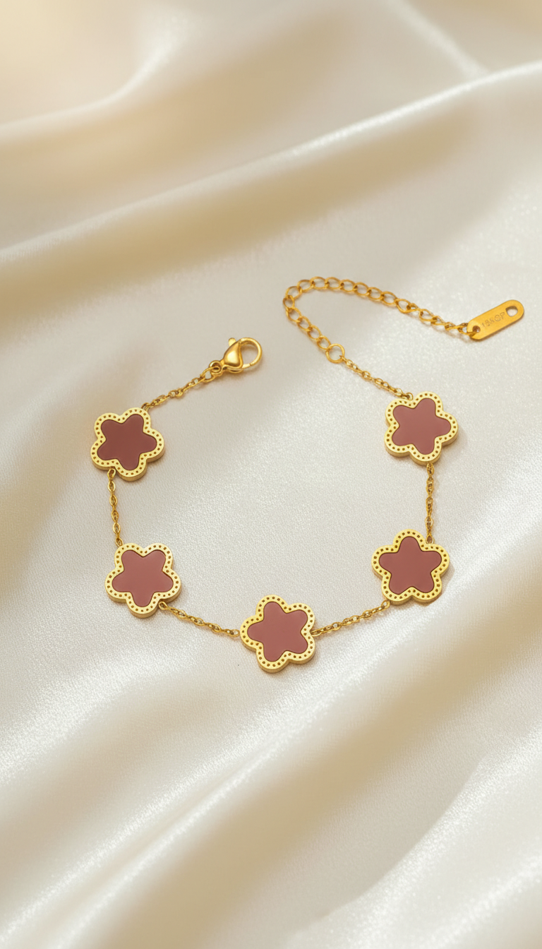 Gold bracelet with five dusty rose enamel clover charms on satin background