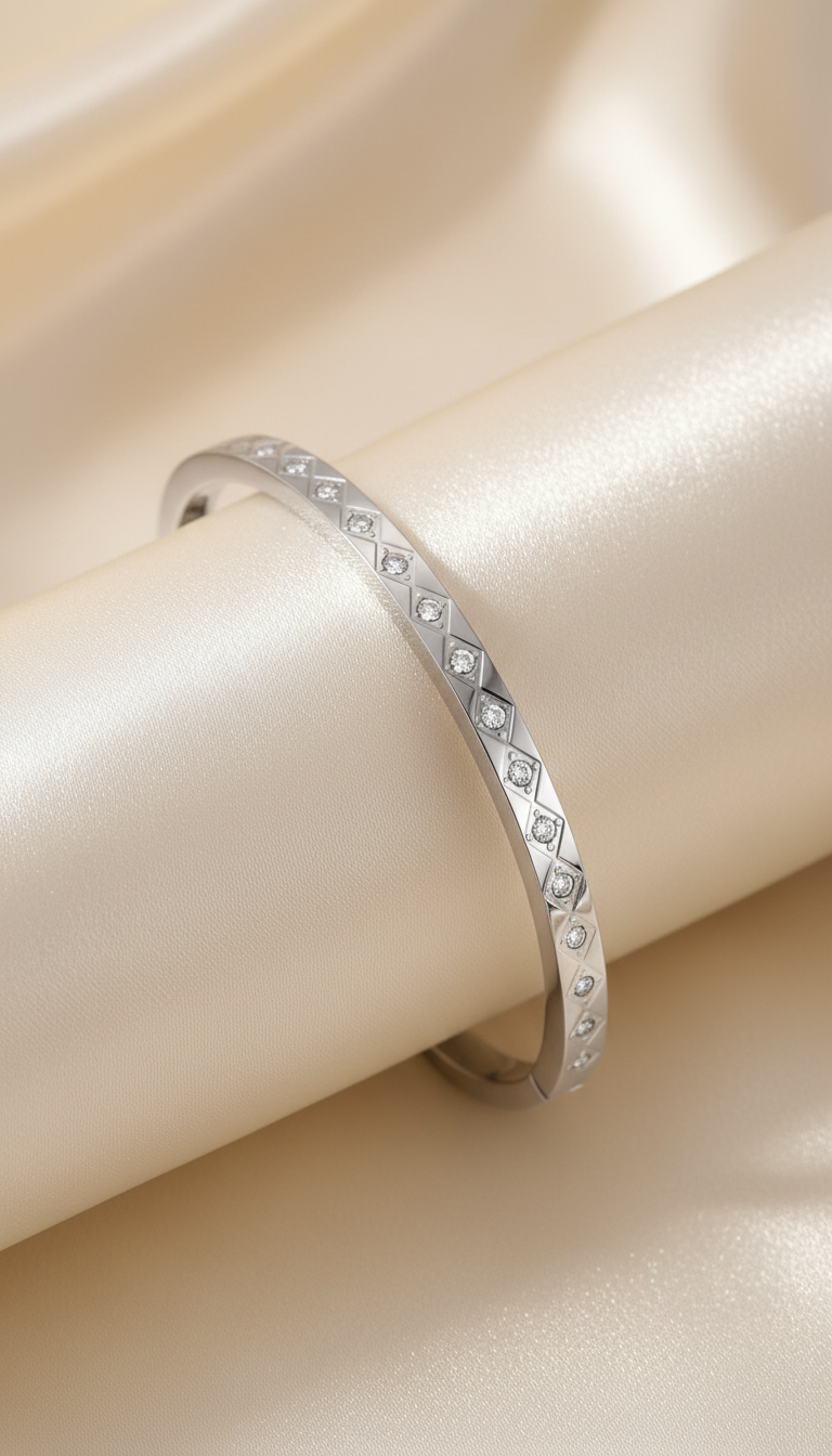 Silver bangle bracelet with engraved diamond grid pattern and cubic zirconia stones on satin background